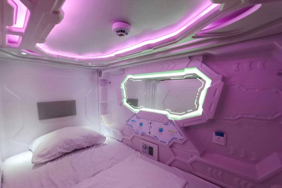 Een futuristische kamer met een bed, een bedieningspaneel en een spiegelwand.