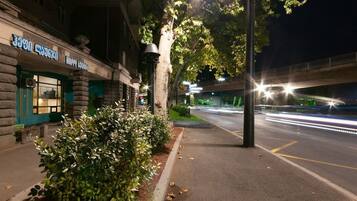 Vista nocturna de una calle con un edificio que dice "Happy Lounge" y una acera bordeada de árboles.