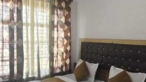 A hotel room with a bed, a ceiling fan, and patterned curtains. - Hotel Sita Kunwar (Prayagraj)