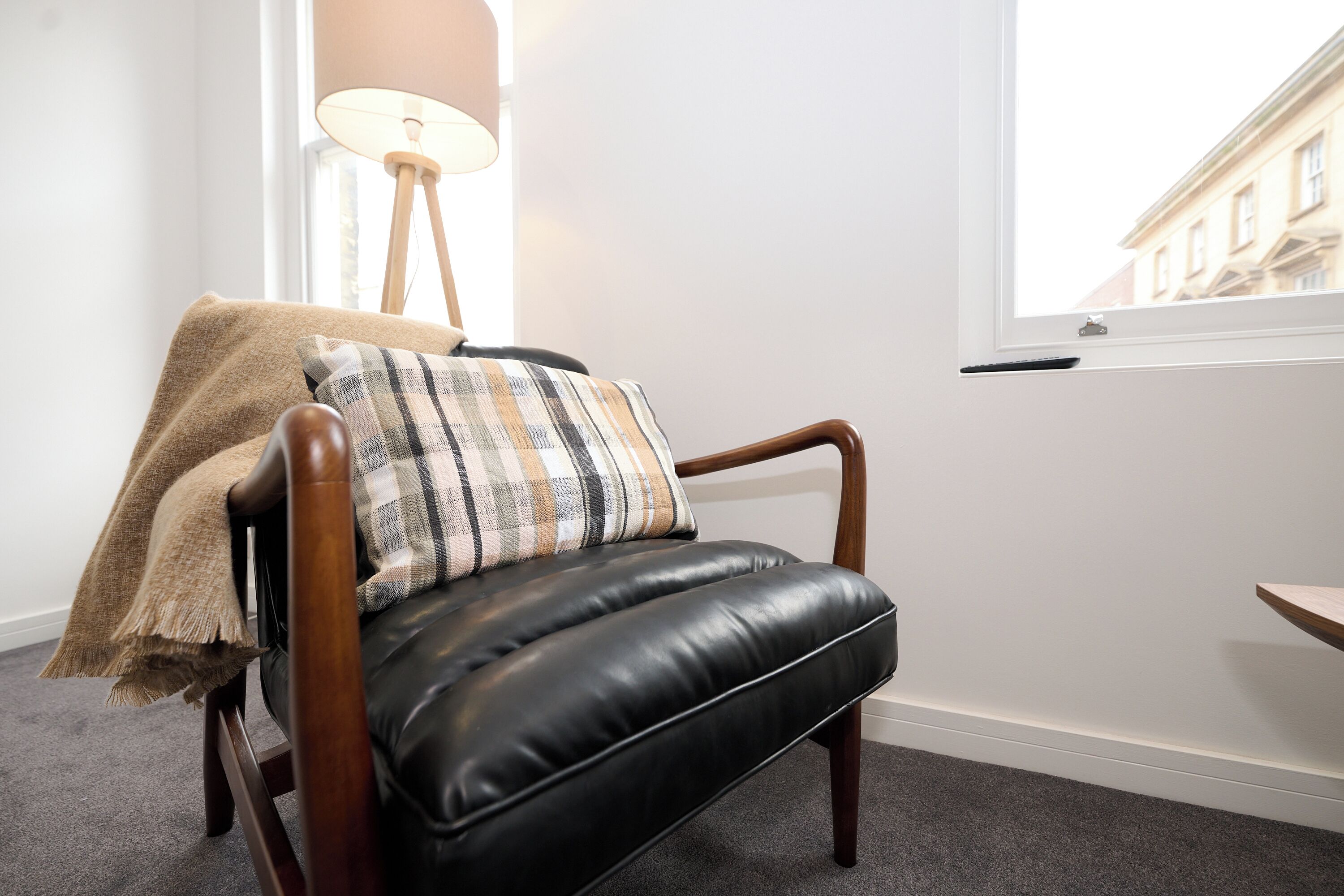 A black leather chair with a plaid pillow and a beige throw blanket.