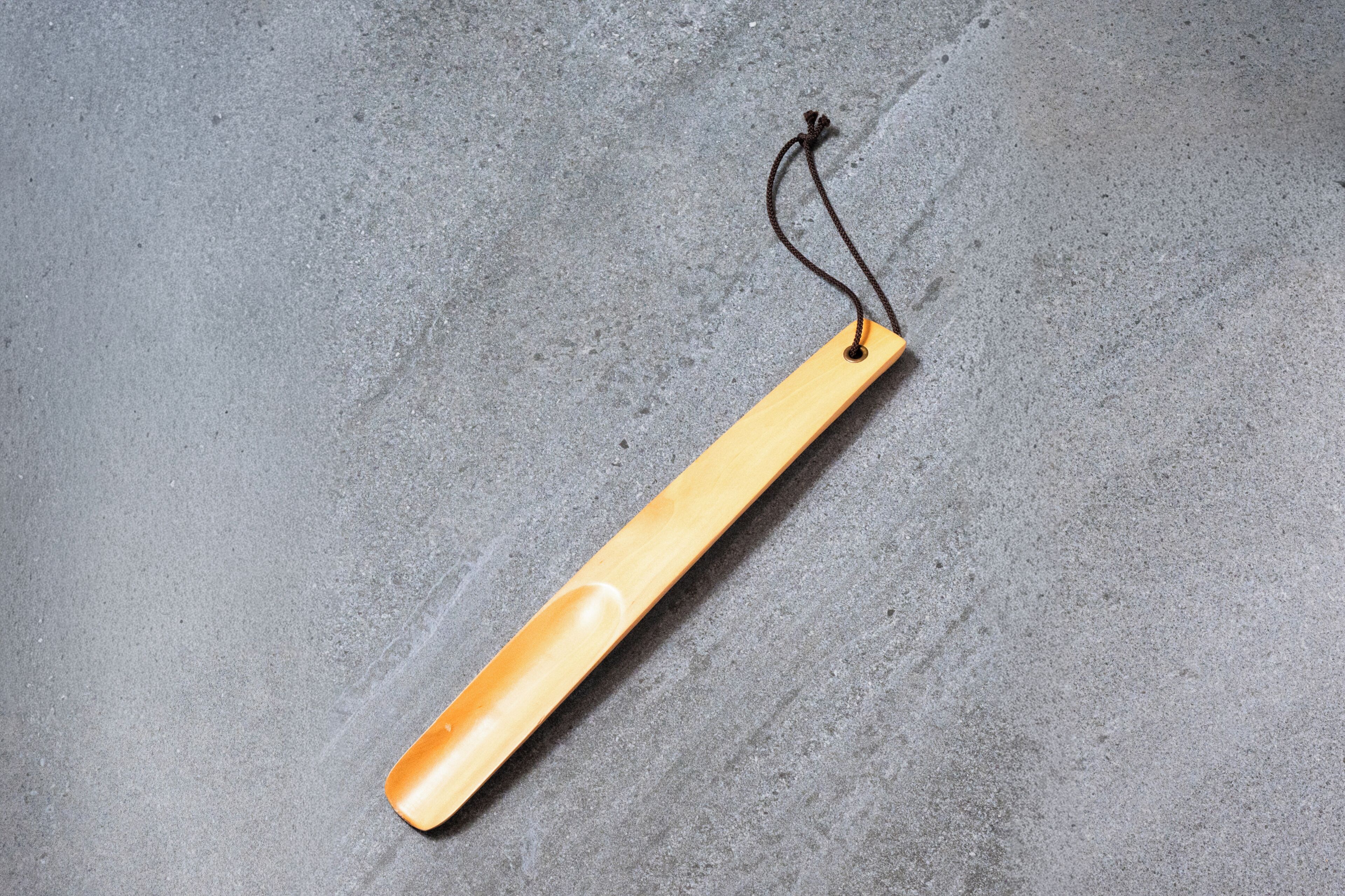 Ein Holzschild mit einer Schnur auf einer grauen, strukturierten Oberfläche.