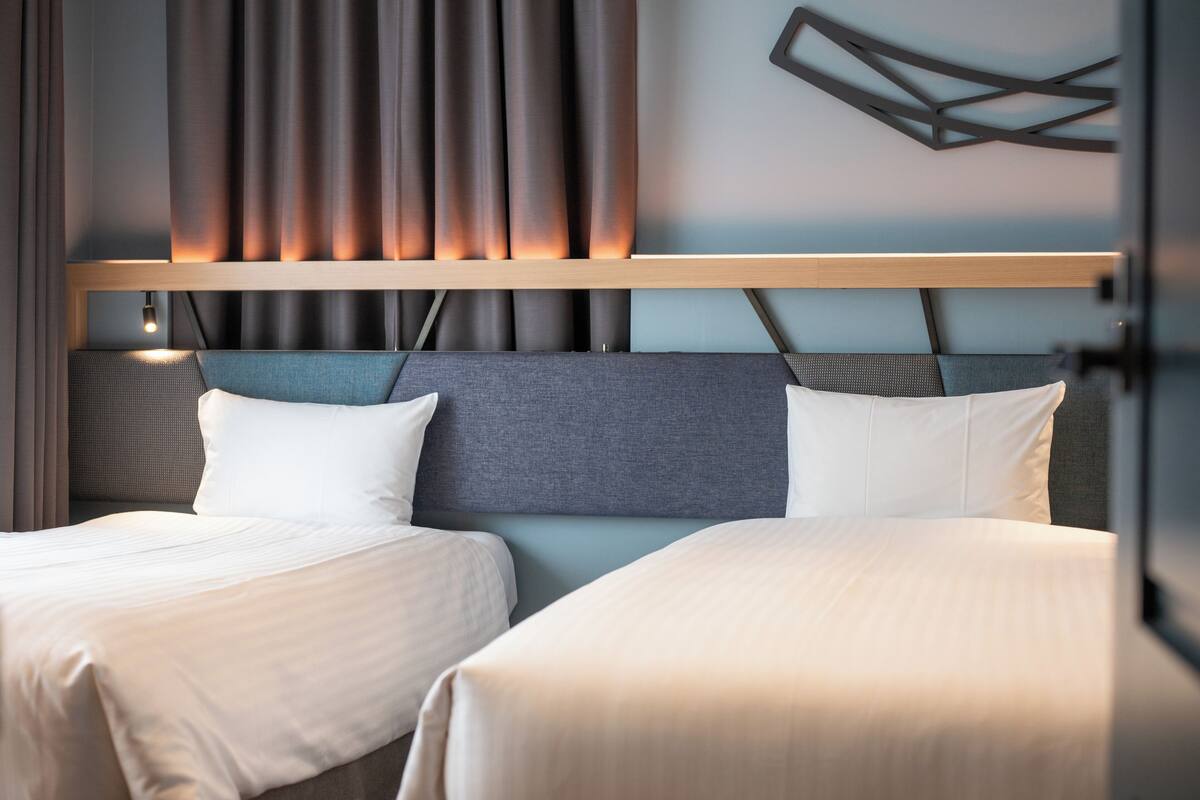 Une chambre d’hôtel avec deux lits, une tête de lit moderne et un luminaire fixé au mur.