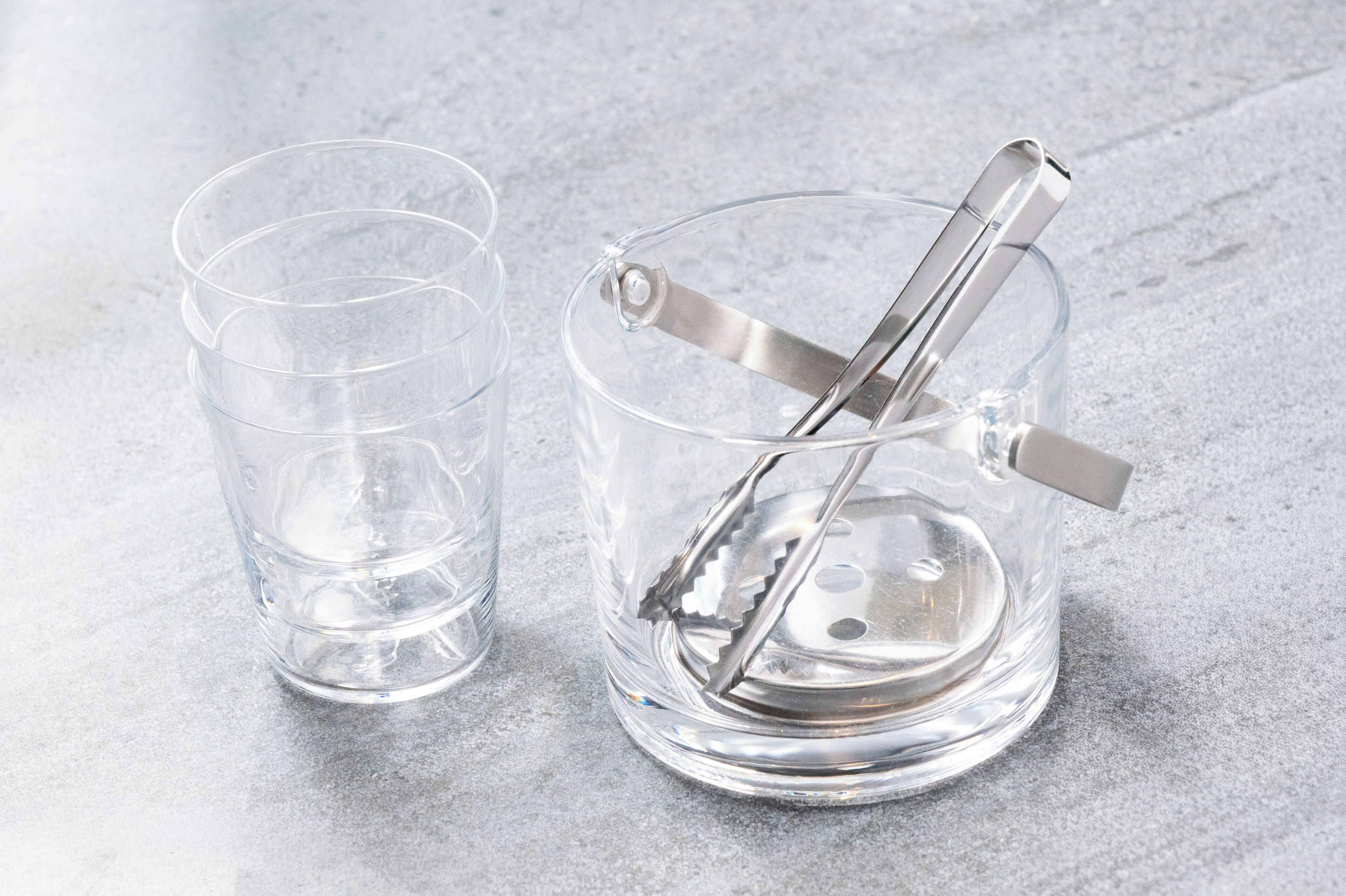Un vaso de vidrio transparente con un rascador de hielo metálico y un espátula para hielo de metal.