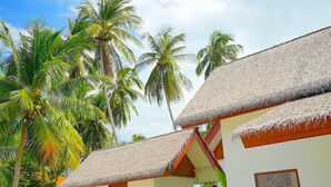 A resort with thatched-roof buildings, palm trees, and a clear sky.