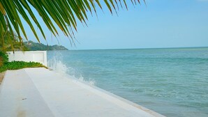 A coastal walkway with a white concrete path, palm trees, and a view of the sea.