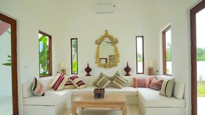 A living room with a white sofa set, a wooden coffee table, and a large ornate mirror.