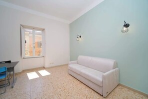 Une pièce avec un canapé blanc, une table à manger avec des chaises, une fenêtre donnant sur un beau paysage et un luminaire fixé au mur.