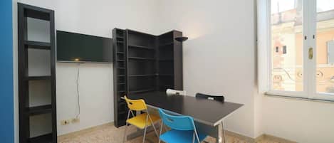 Una habitación con una mesa, sillas, una estantería y una ventana.