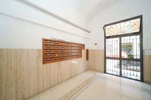 A hallway with a wooden storage unit, a tiled floor, and a large window with a metal gate.