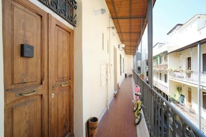 A wooden door, a trash bin, a balcony with a railing, and a building with balconies.