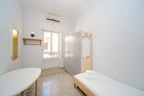 A small, clean room with a bed, a desk, a window, and a wardrobe.