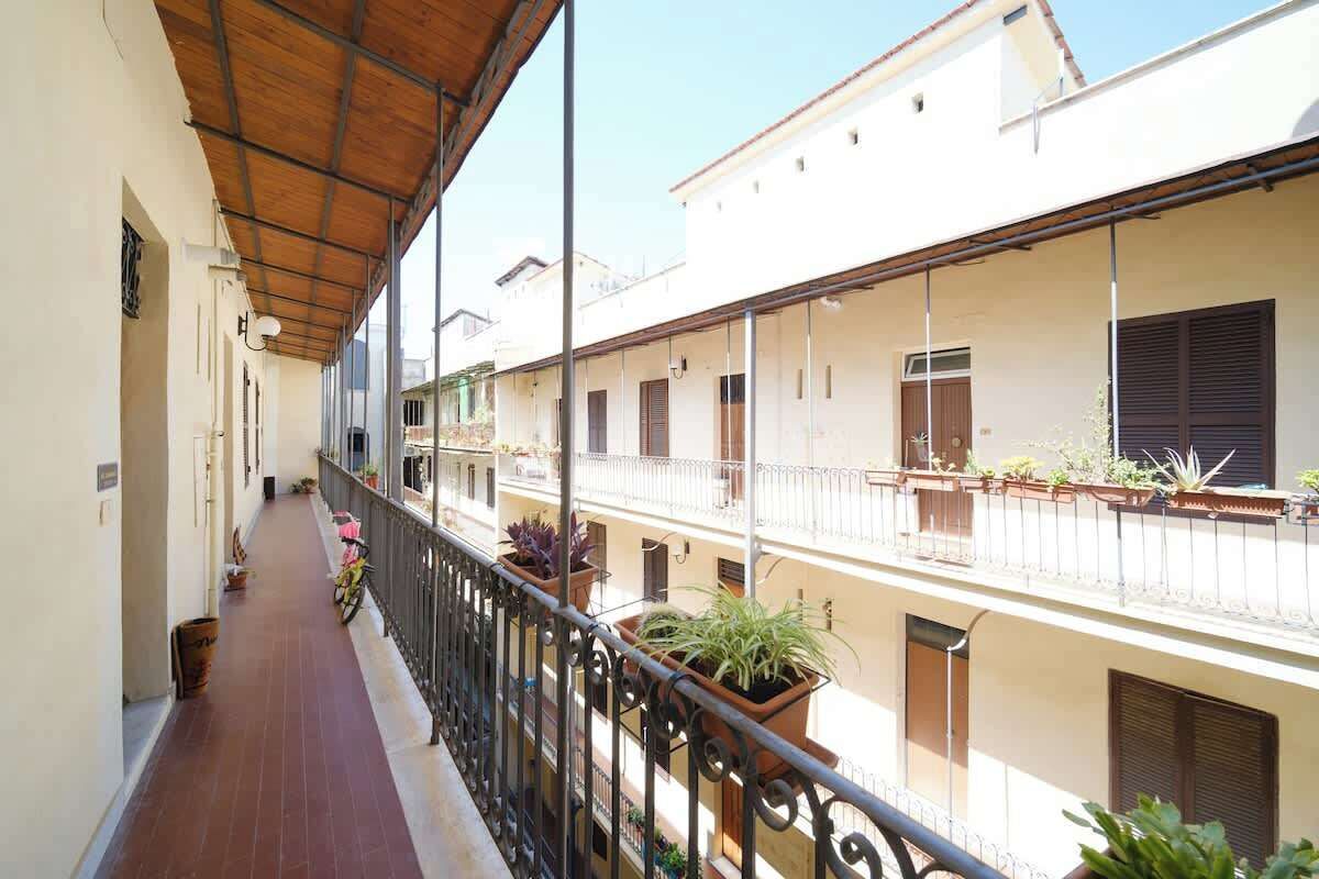A covered balcony with potted plants, a tiled floor, and a view of adjacent buildings.
