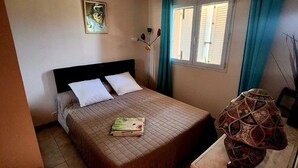 A bedroom with a bed, a chair, a table, a lamp, a window, and a painting on the wall. - Villas with swimming pool Sagone (Vico)