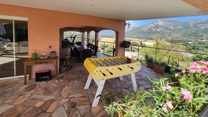 A patio with a foosball table, a dining area, and a view of mountains. - Villas with swimming pool Sagone (Vico)