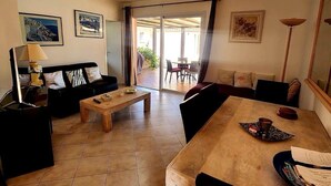 A spacious living room with a sofa set, a wooden coffee table, and a dining table with chairs. There are framed pictures on the walls and a sliding glass door leading to an outdoor area. - Villas with swimming pool Sagone (Vico)