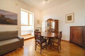 A dining area with a wooden table and chairs, a wooden cabinet, a sofa, and a window with natural light.