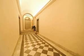 A hallway with a checkered floor, a door at the end, and a staircase leading to an upper level.
