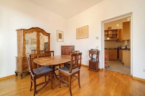 A dining area with a wooden table and chairs, a wooden cabinet, and a kitchen visible through an open doorway.