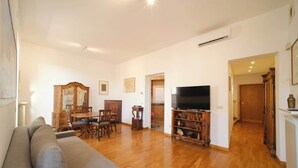 A living room with a sofa, wooden dining table, chairs, a TV, and a cabinet.