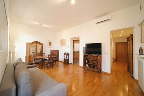A living room with a sofa, wooden dining table, chairs, a TV, and a cabinet.