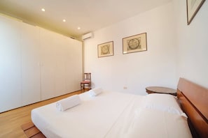 A bedroom with a large bed, a chair, a small table, and two framed pictures on the wall.