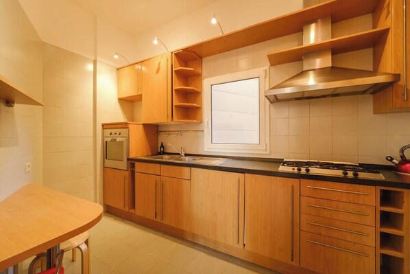 Une cuisine moderne avec des meubles en bois, une cuisinière à gaz, un four encastré et une fenêtre au-dessus de l’évier.