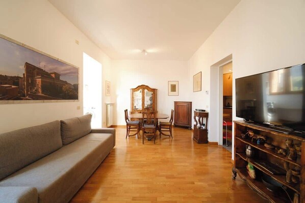A living room with a sofa, dining table, chairs, a TV, and a wooden cabinet.