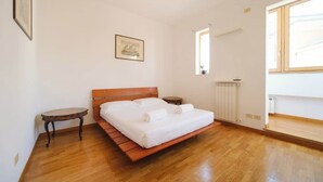 Een slaapkamer met een houten bed, een klein tafeltje, een radiator en een raam.