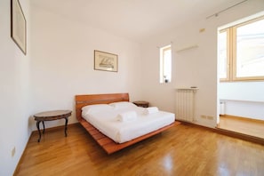 A bedroom with a wooden bed, a small table, a radiator, and a window.