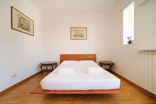 A bedroom with a wooden bed, two bedside tables, a window, and two framed pictures on the wall.
