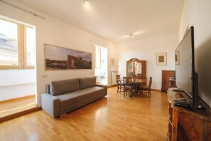 A living room with a sofa, dining table, chairs, a television, and artwork on the walls.