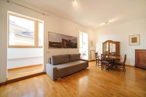 A spacious room with hardwood flooring, a gray sofa, a dining table with chairs, and a wooden cabinet.