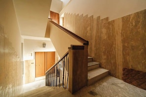 Un escalier avec des marches en bois et une rampe en métal, menant à une pièce dotée d’une porte en bois et d’un luminaire.
