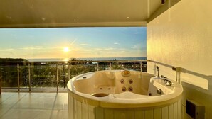 Een hottub op een balkon met uitzicht op zee en de stad tijdens zonsondergang.