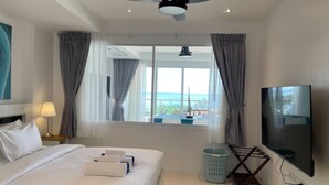 Een hotelkamer met een bed, een televisie, een plafondventilator, een raam met gordijnen en uitzicht op de oceaan.
