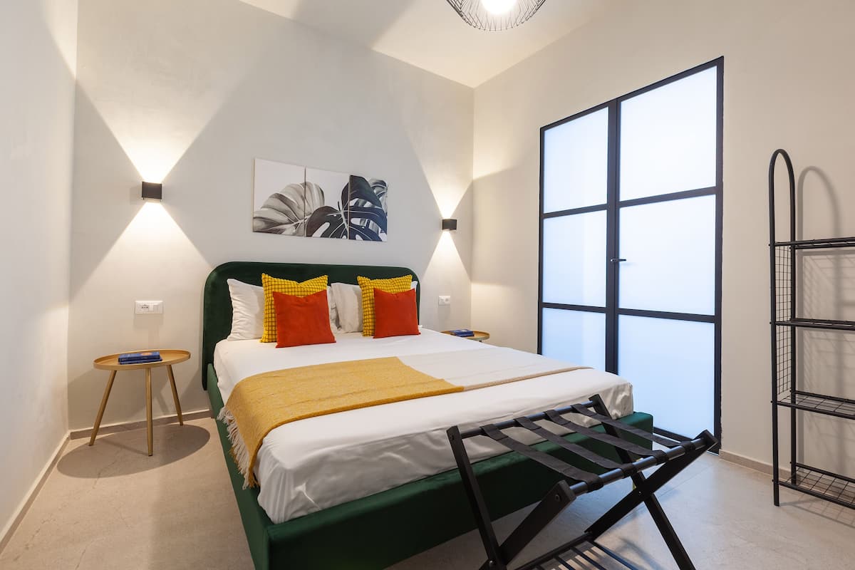 Une chambre à coucher bien rangée, avec un lit, des tables de chevet, une tête de lit verte et une grande fenêtre.