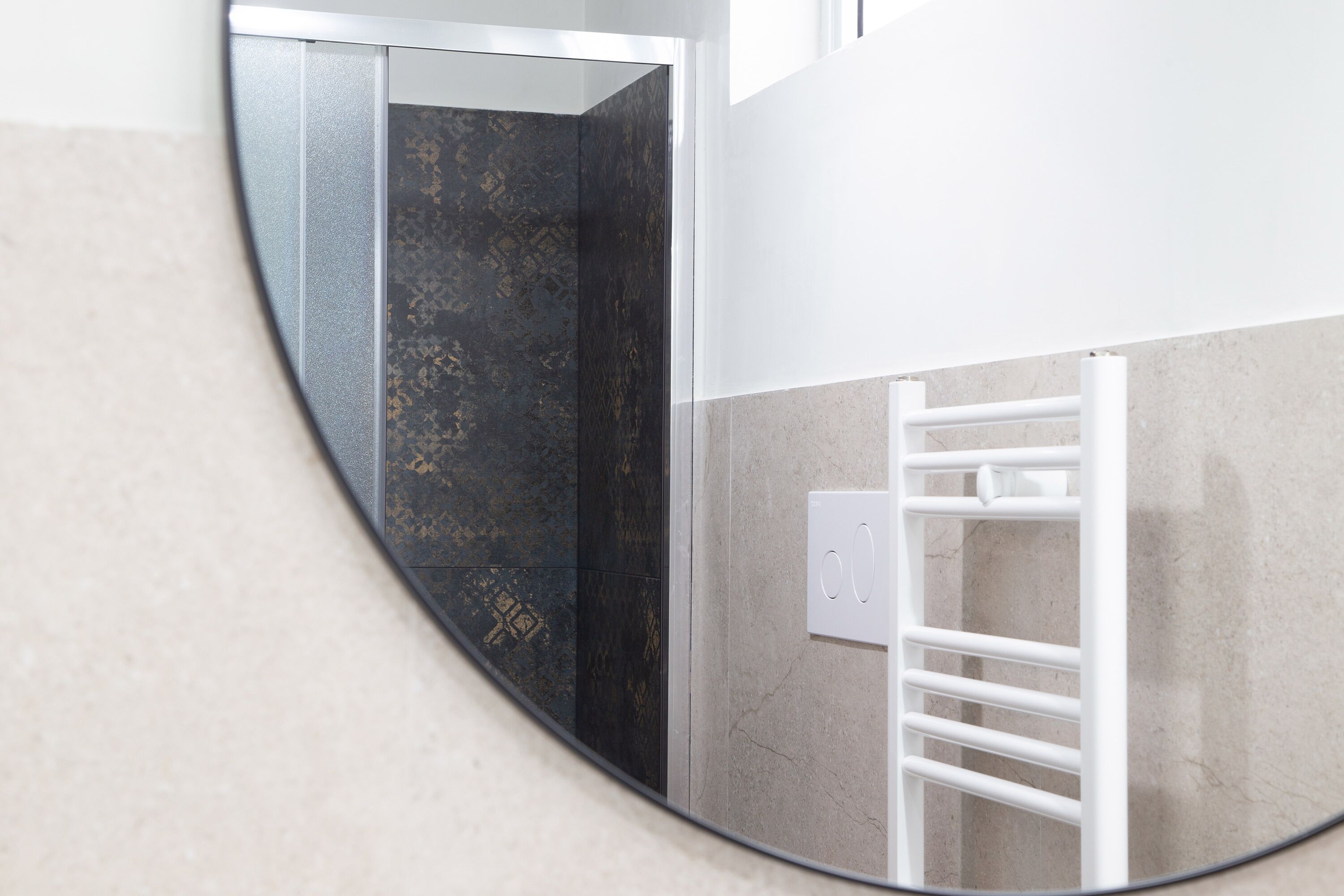 Une salle de bain avec un miroir rond, un porte-serviettes et un mur orné d’un motif texturé.