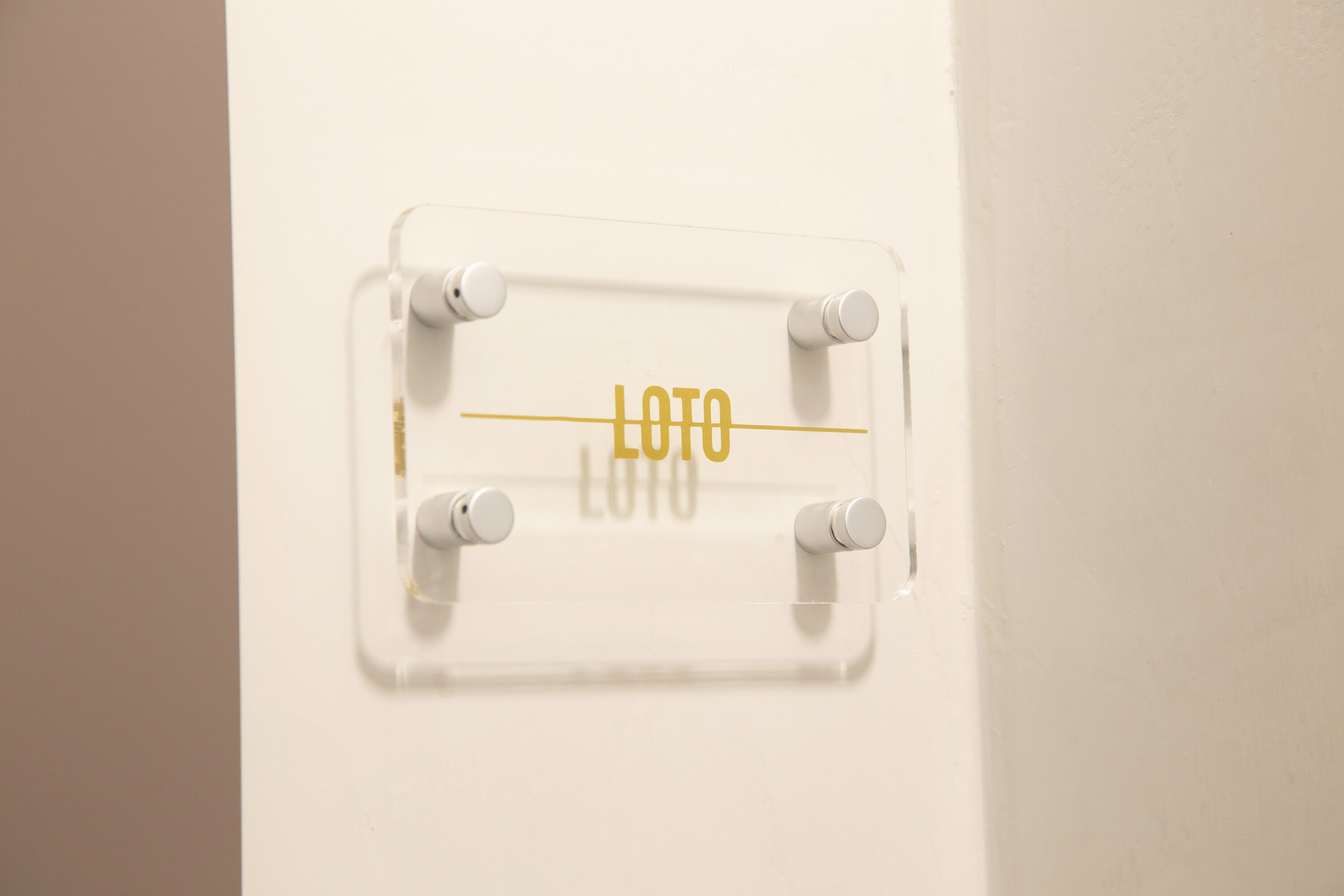 Un letrero de plástico transparente con la palabra 'LOTO' en una pared blanca.