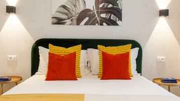 Una cama con cabecera tapizada en verde, dos almohadas con estampado amarillo y rojo, y una colcha blanca.