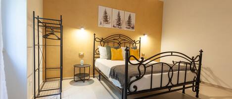 A bedroom with a metal bed frame, a bedside table, a hanging clothes rack, and wall-mounted artwork.