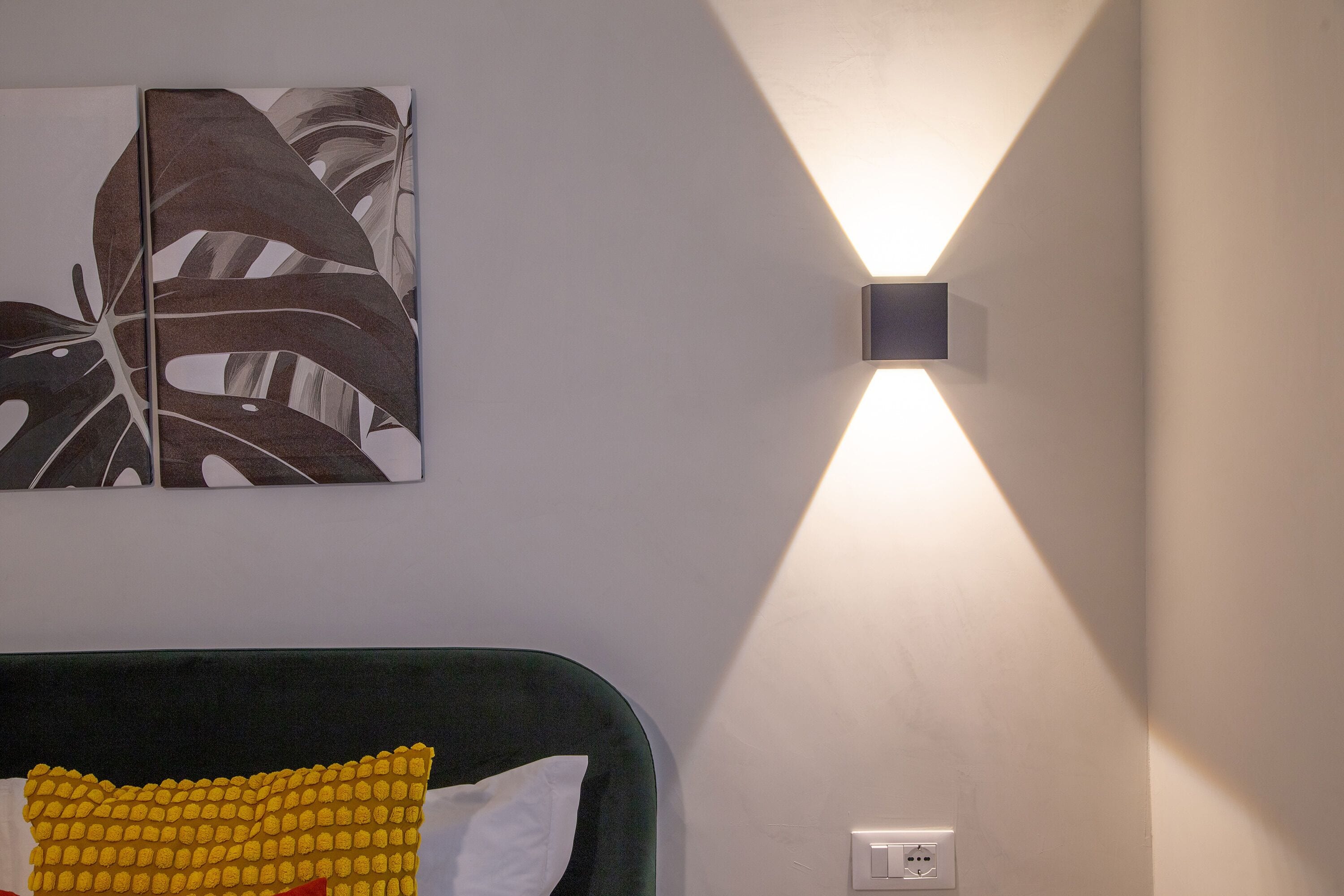 A room with a bed, a wall-mounted light fixture, and a piece of wall art.