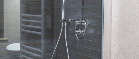 Ducha con cerramiento de vidrio, accesorios cromados y un perchero.