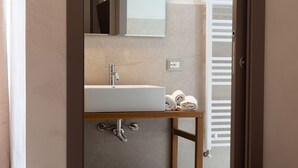 A bathroom with a white sink, a mirror above it, and a towel rack with towels. - Malva Rooms (Agrigento)