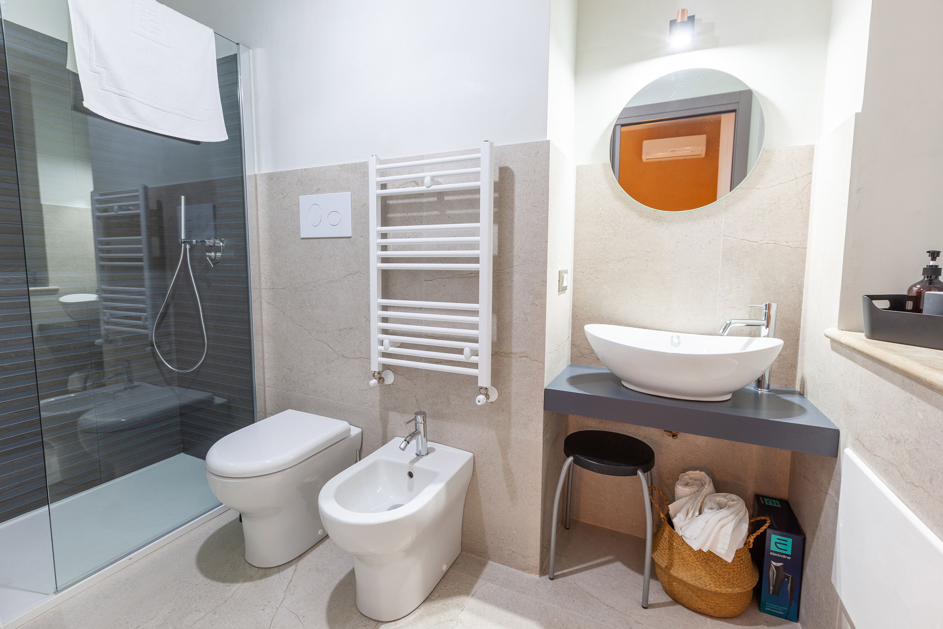 A modern bathroom with a glass shower enclosure, a toilet, bidet, and a sink with a mirror above.