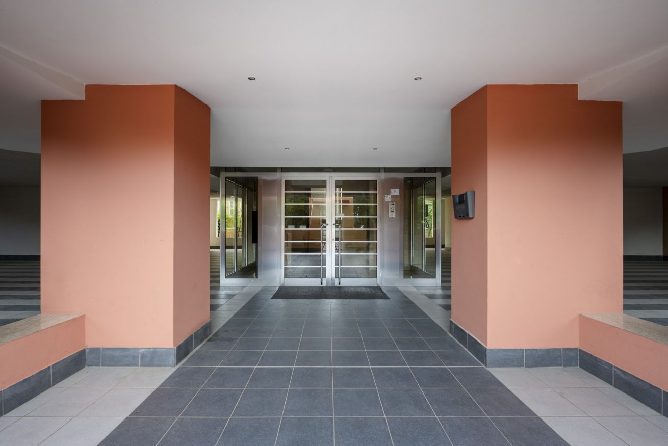 A spacious lobby with a tiled floor, glass doors, and orange walls.