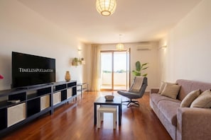 Una sala de estar moderna con una televisión de pantalla plana, un sofá, una butaca, una mesita y un amplio ventanal con vistas.