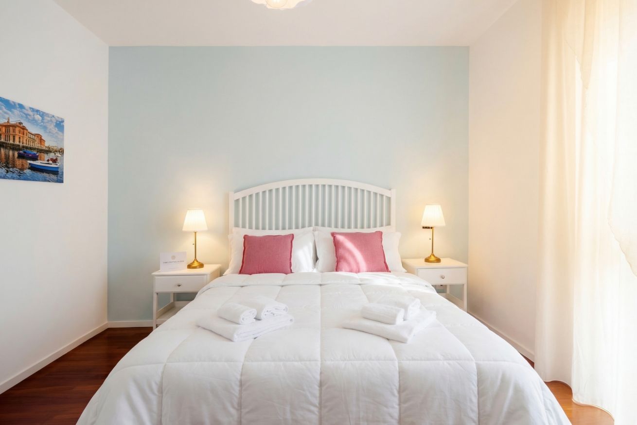 A hotel room with a bed, two bedside tables, a headboard, and a painting on the wall.