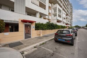 Un immeuble résidentiel à plusieurs étages, doté de balcons, d’une entrée sécurisée et de voitures garées le long de la rue.