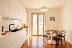 Une cuisine moderne avec des meubles blancs, un évier noir et un coin repas comprenant une table ronde et quatre chaises.