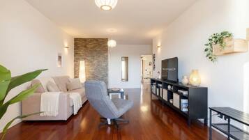 A modern living room with a sofa, armchair, wooden flooring, a TV, and a bookshelf.